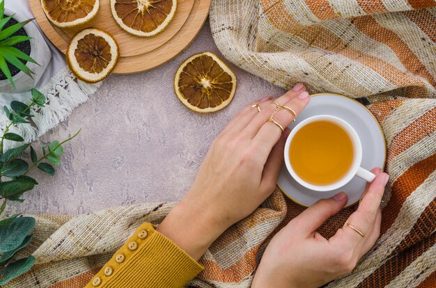 An overhead view of woman's hand holding the herbal tea cup and dried lemon on textured backdrop