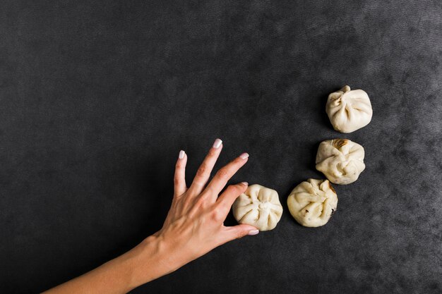 An overhead view of woman's hand holding steam dumplings on black textured background