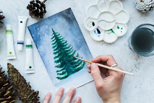 An overhead view of a woman's hand painting christmas tree on canvas