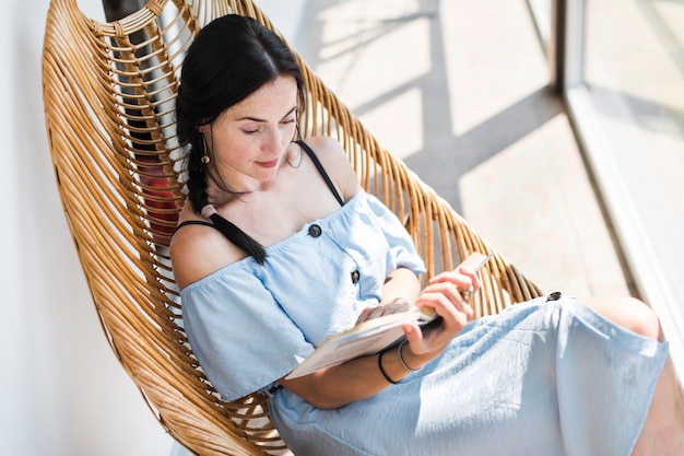 An overhead view of woman sitting on wooden chair reading book