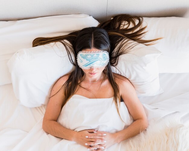 An overhead view of woman wearing eye mask sleeping on bed