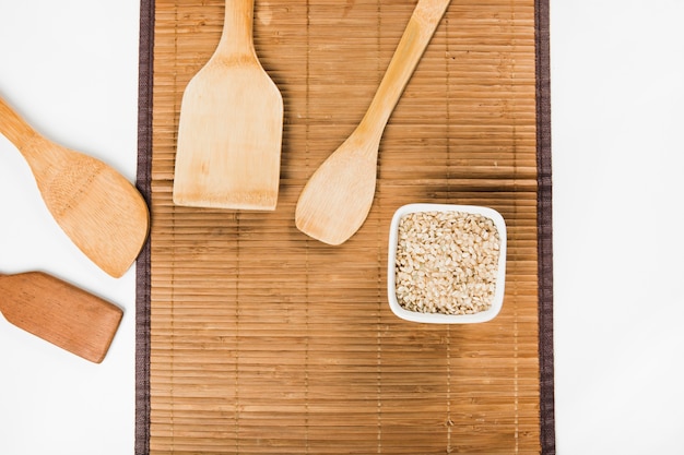 An overhead view of wooden spatulas with uncooked brown rice bowl on placemat