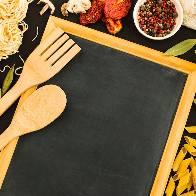 An overhead view of wooden spoon and spatula on blank slate with pasta ingredients