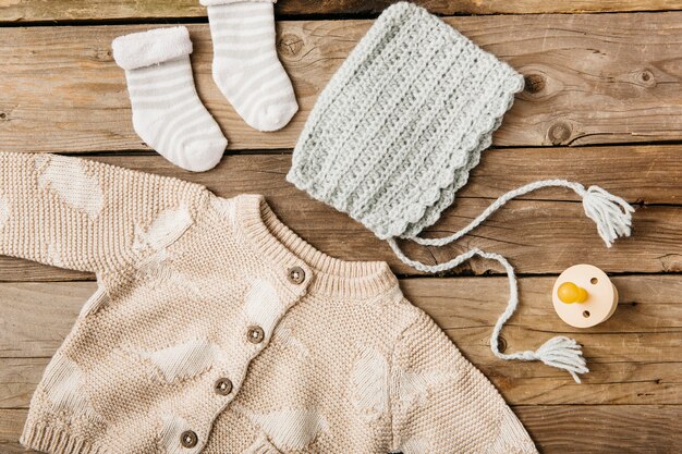 An overhead view of woolen baby's clothing with pacifier on wooden table