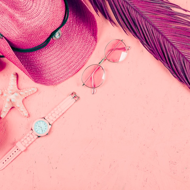 Вид сверху наручных часов; солнцезащитные очки; шапка; листья и морские звезды на розовом фоне текстурированных