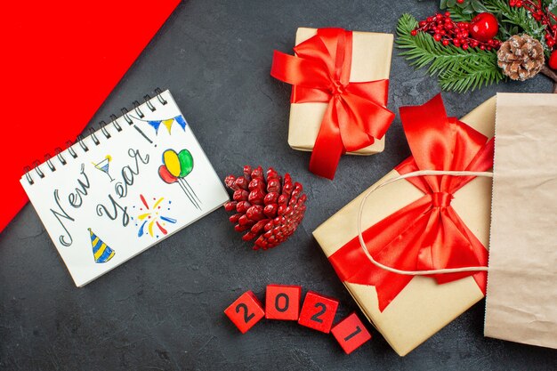 Вид сверху на блокнот рождественского настроения с новогодними рисунками, хвойными шишками и номерами подарочных еловых веток на темном столе