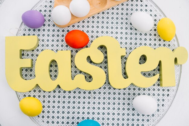 An overhead view of yellow easter word with colorful eggs on white round table