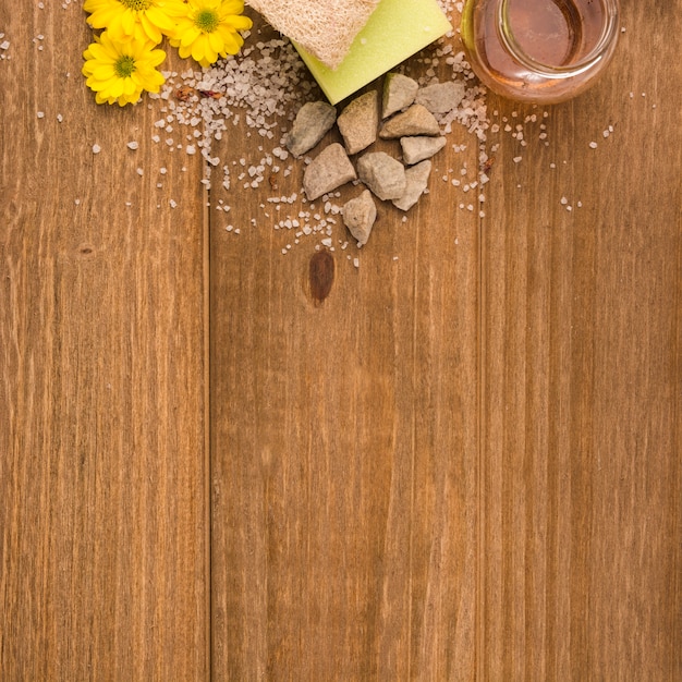 Foto gratuita una vista dall'alto di fiori gialli; sale; pietre; spugna; bottiglia di luffa e miele su fondo strutturato in legno