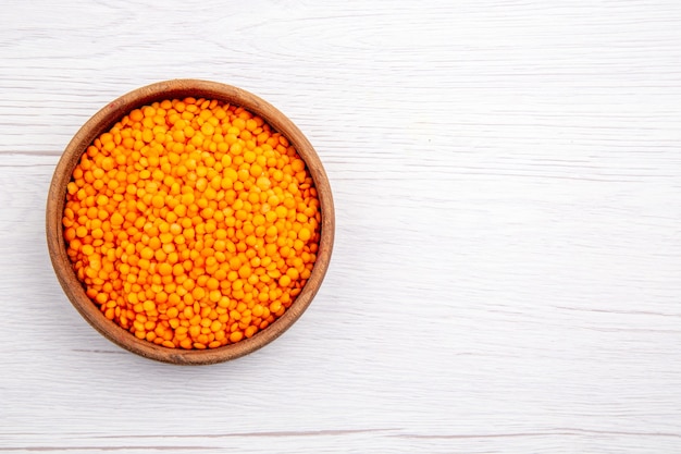 Overhead view of yellow lentils in a brown bowl on the right side on white background