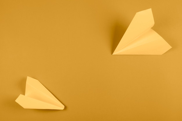 An overhead view of yellow paper airplane on bright colored background