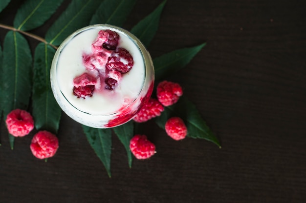An overhead view of yogurt smoothie with raspberries on leaves against black background