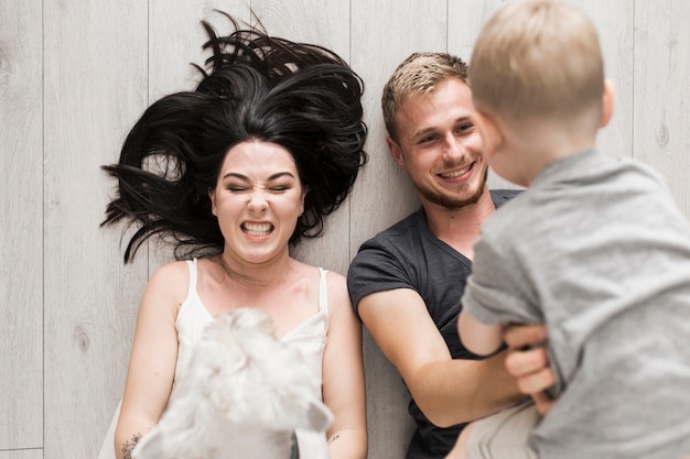 Free photo an overhead view of young couple lying on hardwood floor carrying their little son and dog