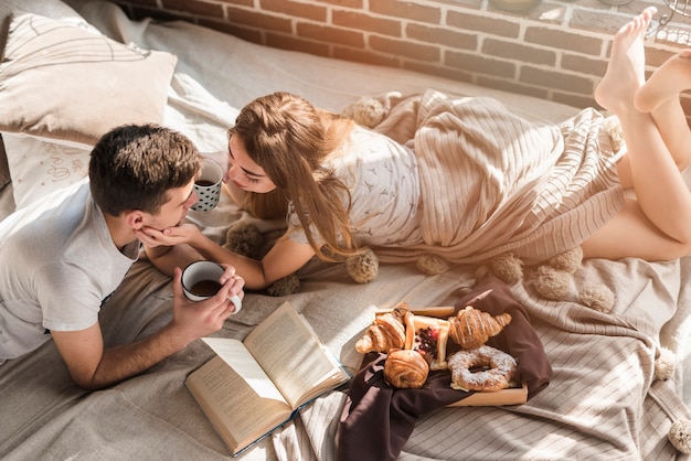 An overhead view of young couple lying on messy bed with breakfast on bed