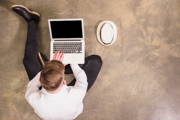 Free photo an overhead view of a young man sitting on concrete floor using digital tablet