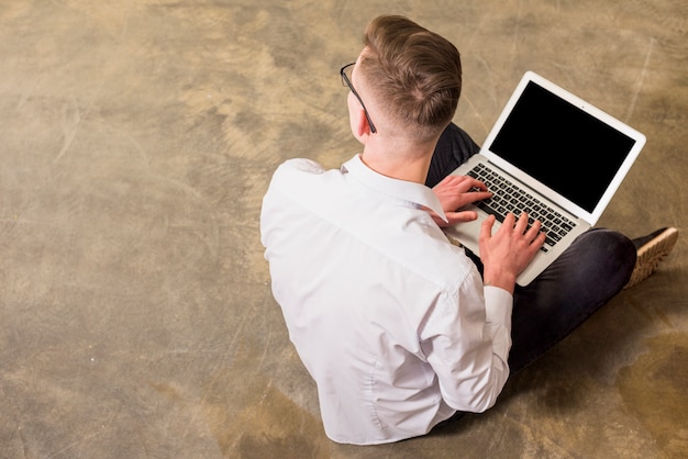 An overhead view of young man sitting on concrete floor using laptop