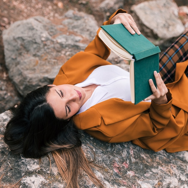 An overhead view of a young woman lying on the rock reading book