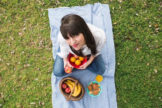 Foto gratuita una vista aerea di una giovane donna con frutta al picnic nel parco