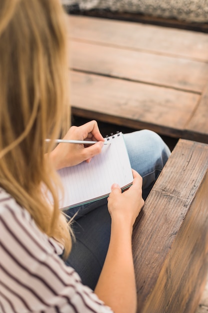 Overhead view of young woman writing on notebook with pencil