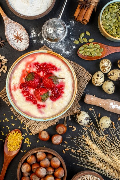 Overhead view of yummy breakfast served with strawberries jam in a bowl and honey eggs flour sugar spoons on dark color background