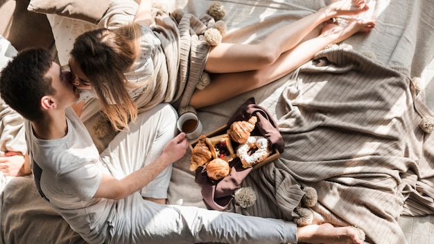 An overhead of young couple kissing to each other while having breakfast on bed