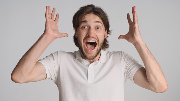 Overjoyed attractive brunette man exclaiming loudly keeping mouth open clenched fists and rejoicing of success over white background