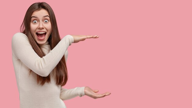 Overjoyed attractive woman shows size of something big, surprised by huge object