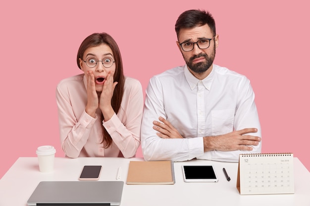 Overjoyed beautiful lady exclaims with happiness, opens mouth, expresses good emotions after promotion, discontent unshaven executive man in white shirt