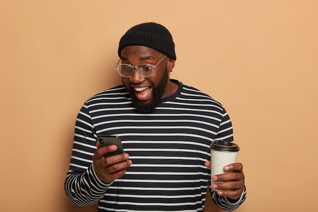 Overjoyed dark skinned guy concentrated in smartphone