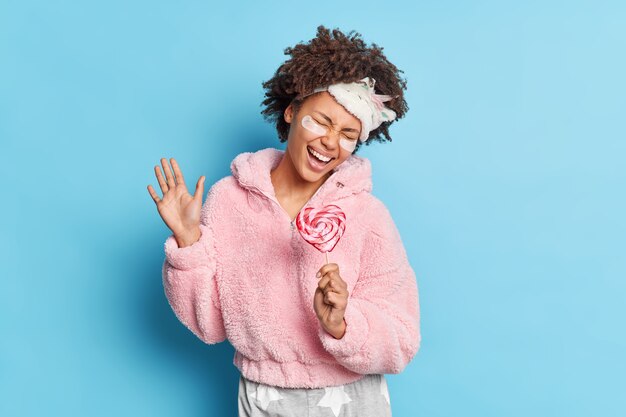 Overjoyed dark skinned woman sings loudly holds delicious candy as if microphone