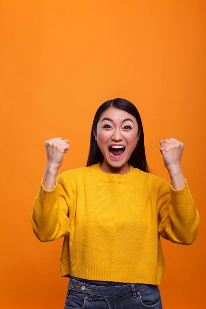 Overjoyed excited confident beautiful woman model celebrating in triumph successful results. Strong optimistic young adult asian woman laughing heartily while winning video game.