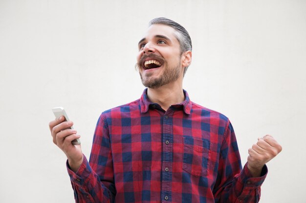 Overjoyed excited man with cellphone making winner gesture