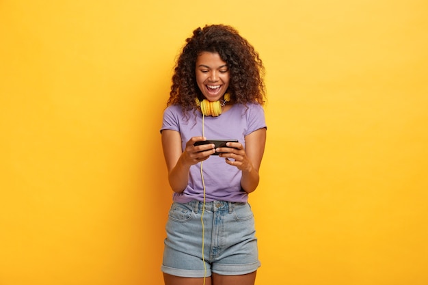 Обрадованная женщина играет на смартфоне, увлечена онлайн-играми, свободное время проводит с современными технологиями.