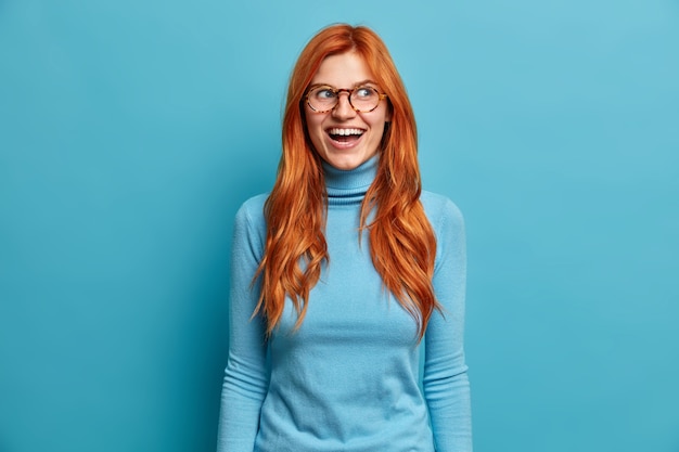 ヨーロッパの外観を持つ大喜びの生姜の若い女性は大声で笑い、楽しみを持っており、光学メガネのカジュアルなタートルネックを身に着けている素敵なイベントを喜んでいます。