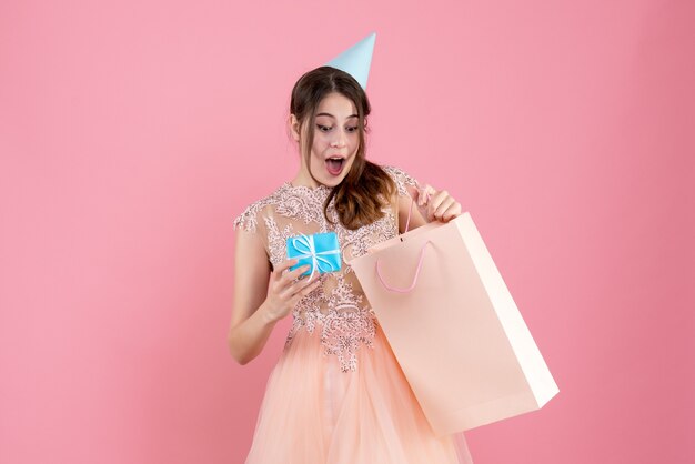 overjoyed girl with party cap looking at her gift on pink