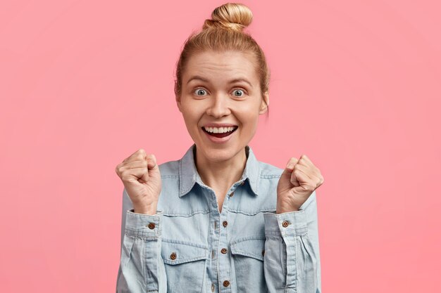 Overjoyed pretty female with blonde hair tied in bun