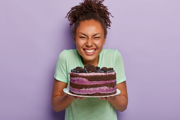大喜びのきれいな女性は、大きなおいしい食欲をそそるケーキでプレートを保持します