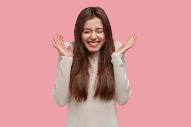 Overjoyed smiling lady spreads palms, expresses joy and happiness, asks to stop telling funny stories, keeps eyes closed