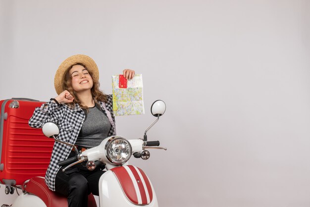 overjoyed young woman on moped holding card and map on grey