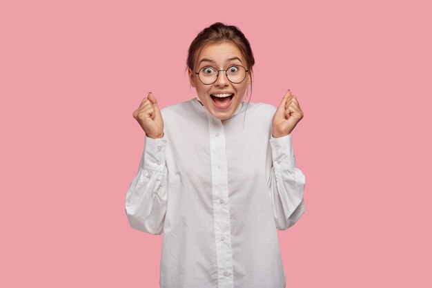 Overjoyed young woman with glasses posing against the pink wall