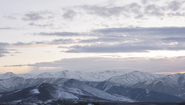 雪に覆われた山々と曇り空に沈む夕日の美しい景色を見渡す