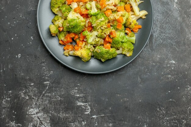 Overview of healthy meal with brocoli and carrots on a black plate on gray table