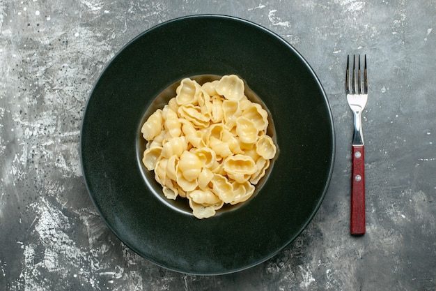 Обзорный вид вкусных конкильи на черной тарелке и ножом на сером фоне