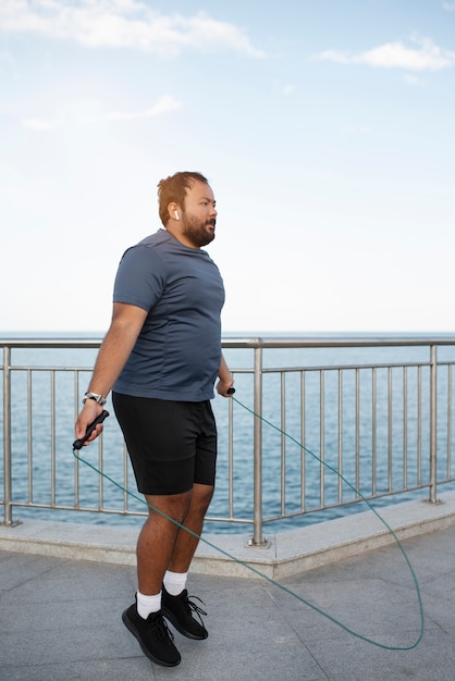 Overweight man exercising with jumping rope outdoors