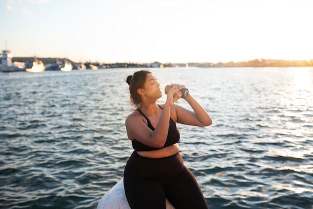 Женщина с избыточным весом получает гидратацию водой после тренировки на открытом воздухе