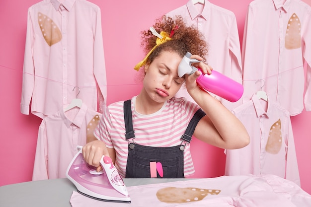 Foto gratuita la governante della donna assonnata oberata di lavoro si asciuga la fronte si sente affaticata mentre fa i lavori di casa stira i vestiti fa le faccende domestiche tiene il flacone spray camicia bruciata avere fretta di finire tutto.