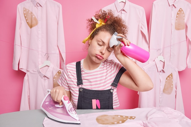 Overworked sleepy woman housekeeper wipes forehead feels fatigue while doing housework irons clothes does domestic chores holds spray bottle burned shirt being in hurry to finish everything.