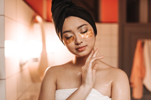 Pacified woman after shower in towel poses with eye patches