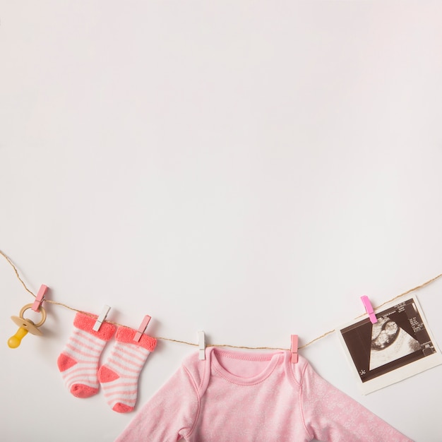 Free photo pacifier; sonography picture; socks; baby clothing hanging on clothesline over white background