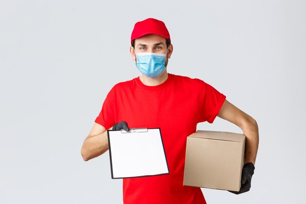 Packages and parcels delivery, covid-19 quarantine delivery, transfer orders. Friendly courier in red uniform, face mask and gloves, holding package box and give clipboard order sign form to client