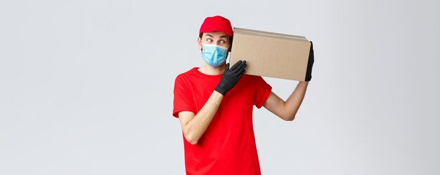 Packages and parcels delivery covid19 quarantine delivery transfer orders Curious courier in red uniform gloves and protective face mask deliver box to client bring order contactless